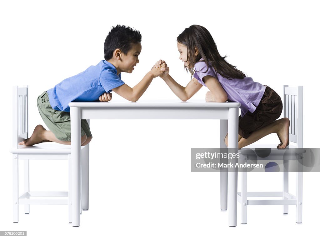 Boy and girl sitting at table arm wrestling
