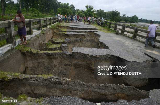 Indian people look at a bridge damaged by torrential rain at Toribari village on the outskirts of Siliguri on July 21,2016. - Continuous rainfall in...