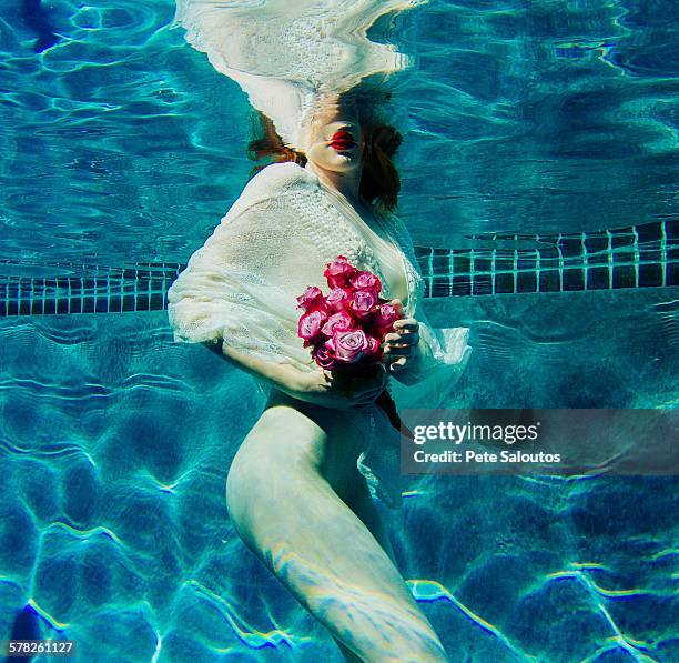 Young woman underwater, wearing thin white shirt and holding flowers