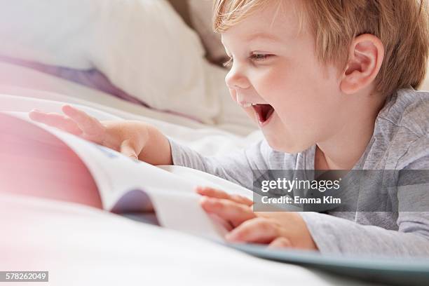 head and shoulders of boy on bed lying on front looking at storybook, laughing - the end story stock pictures, royalty-free photos & images