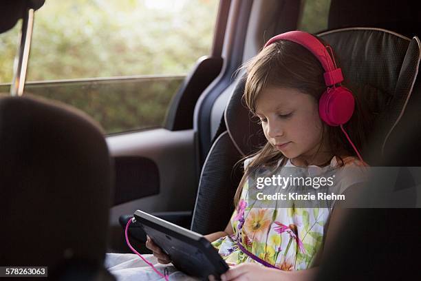 girl wearing pink headphones using digital tablet in car - girl in car with ipad stock pictures, royalty-free photos & images