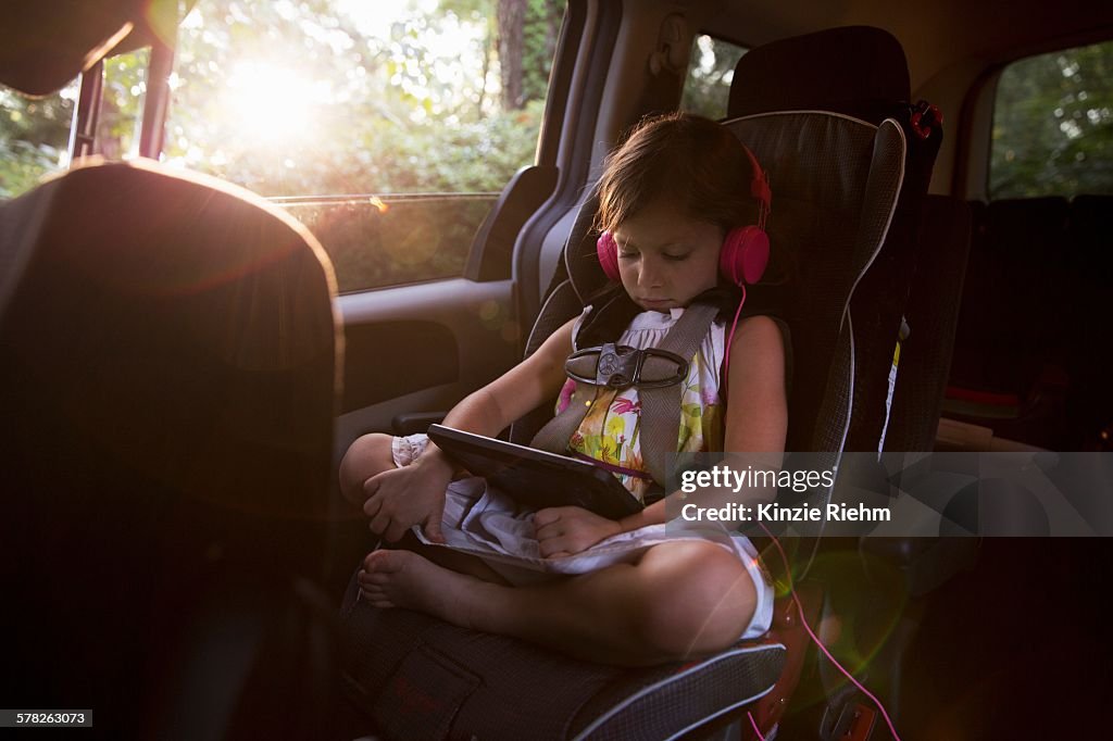 Girl wearing headphones using digital tablet in car back seat