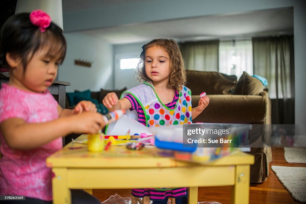 Two young girls sitting at table, making art, using paint