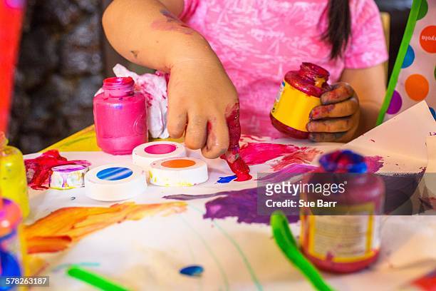 girl sitting at table, making art, using paint, focus on artwork - vingerverf stockfoto's en -beelden
