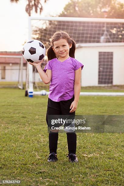 portrait of girl football player holding up football on practice pitch - football pitch bildbanksfoton och bilder