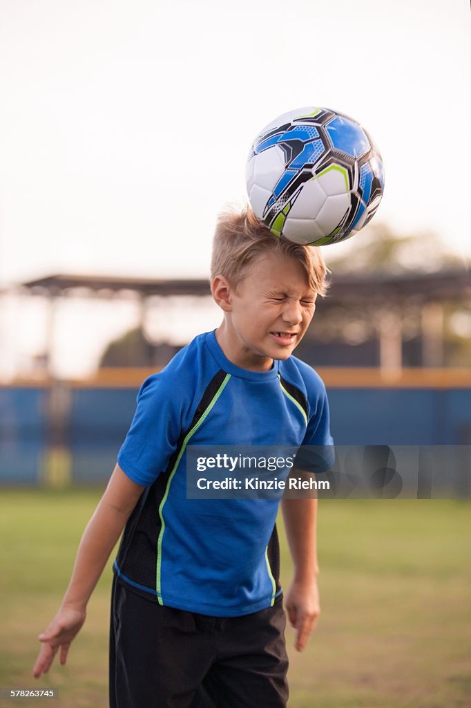 Boy with eyes closed heading football on practice pitch