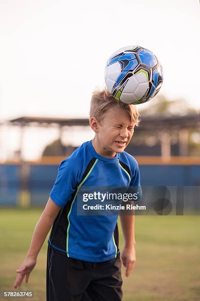 boy with eyes closed heading football on practice pitch - kopfball stock-fotos und bilder