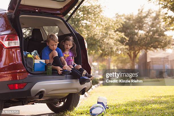 boy and younger sister preparing for football practice whist sitting in car boot - tiersport stock pictures, royalty-free photos & images