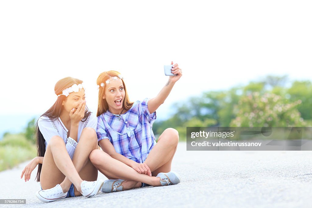Young boho women sitting on country road and making selfie