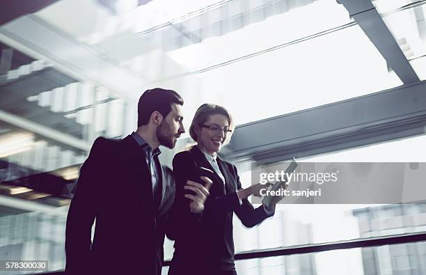 two business coworkers walking along office coridor - man lady phone ipad outside stock pictures, royalty-free photos & images