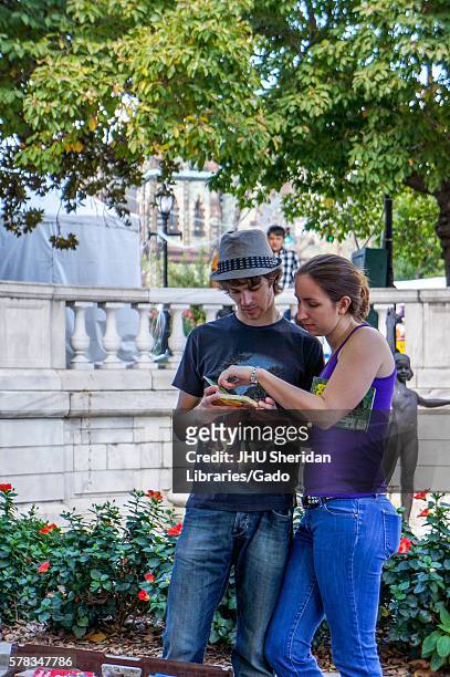 Young couple look at an used book at a vendor stand outside in a park in Mount Vernon at the Baltimore Book Festival, Baltimore, Maryland, 2013. .