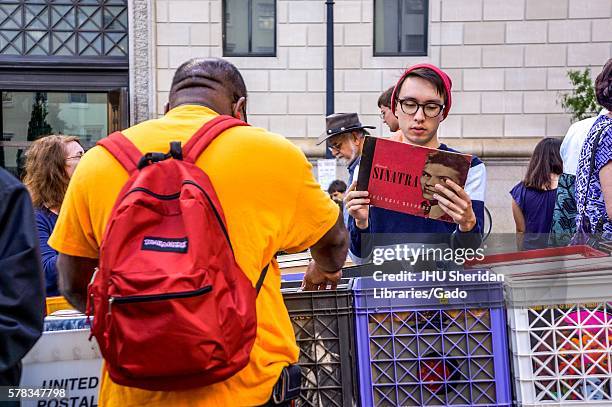 Young man looks at a Frank Sinatra record in front of a bin of records where other people explore at the Baltimore Book Festival, Baltimore,...