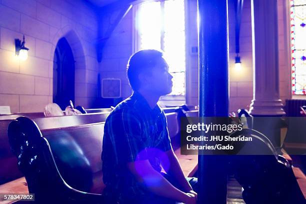 Young man sitting on a pew in a well lit church with stained glass windows at the Baltimore Book Festival, Baltimore, Maryland, September, 2013. .