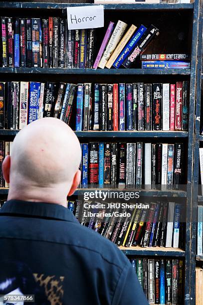 Man with bald head looks up at a shelf of used paperback books labeled "Horror, " during Baltimore Book Festival, Baltimore, Maryland, September,...