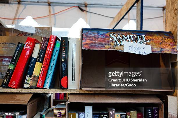 Shelf of used books for sale leaning against an empty beer case, labeled "Modern Fiction, " during Baltimore Book Festival, Baltimore, Maryland,...