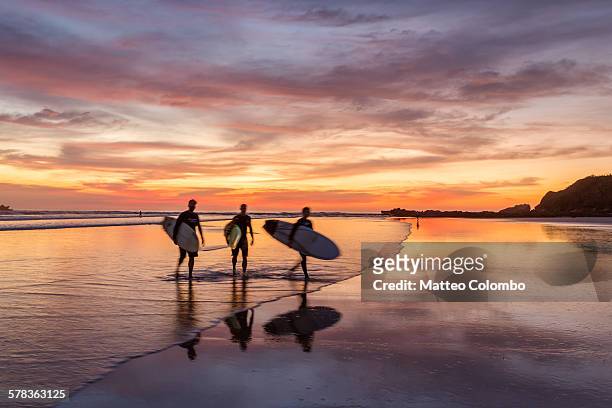 surfers at sunset walking on beach, costa rica - costa rica stock-fotos und bilder