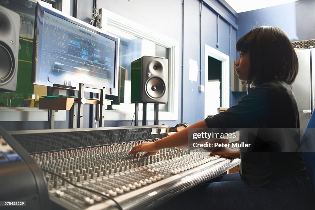 Side view of young woman sitting at mixing desk in recording studio looking at monitor, adjusting controls