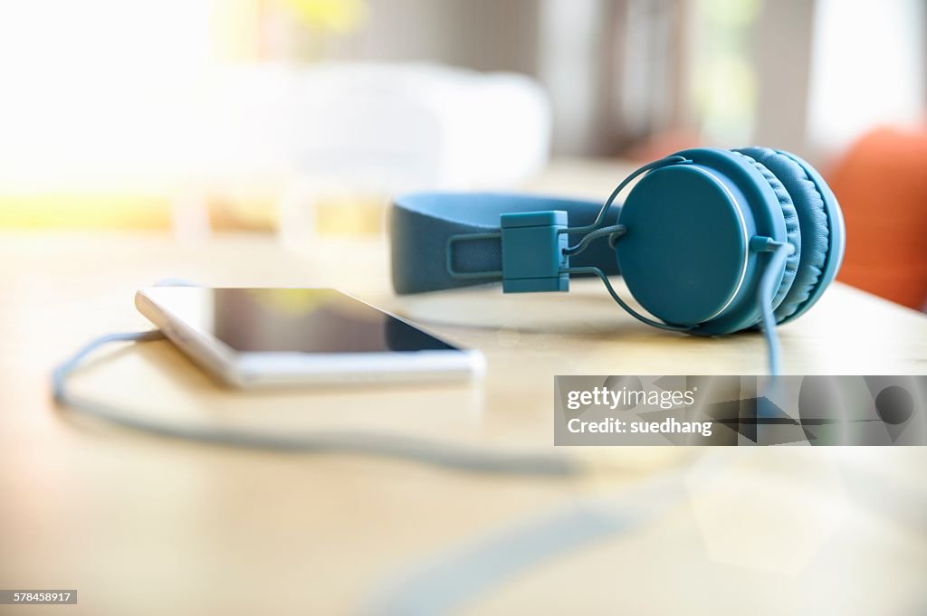 Surface level view of blue headphones attached to smartphone on table