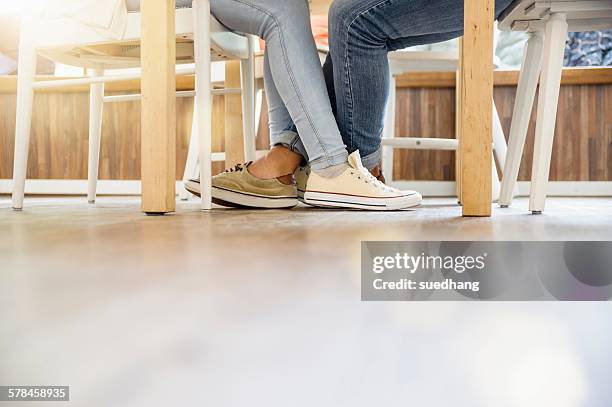 surface level view of couples entwined legs sitting at table face to face - playing footsie stock pictures, royalty-free photos & images