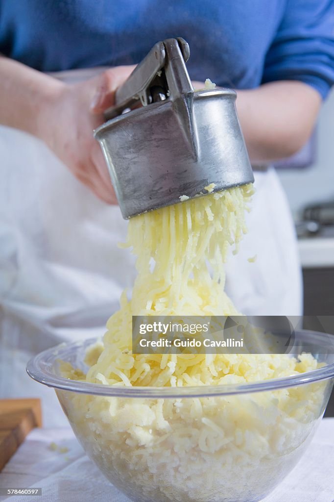 Cropped shot of woman using potato ricer in kitchen