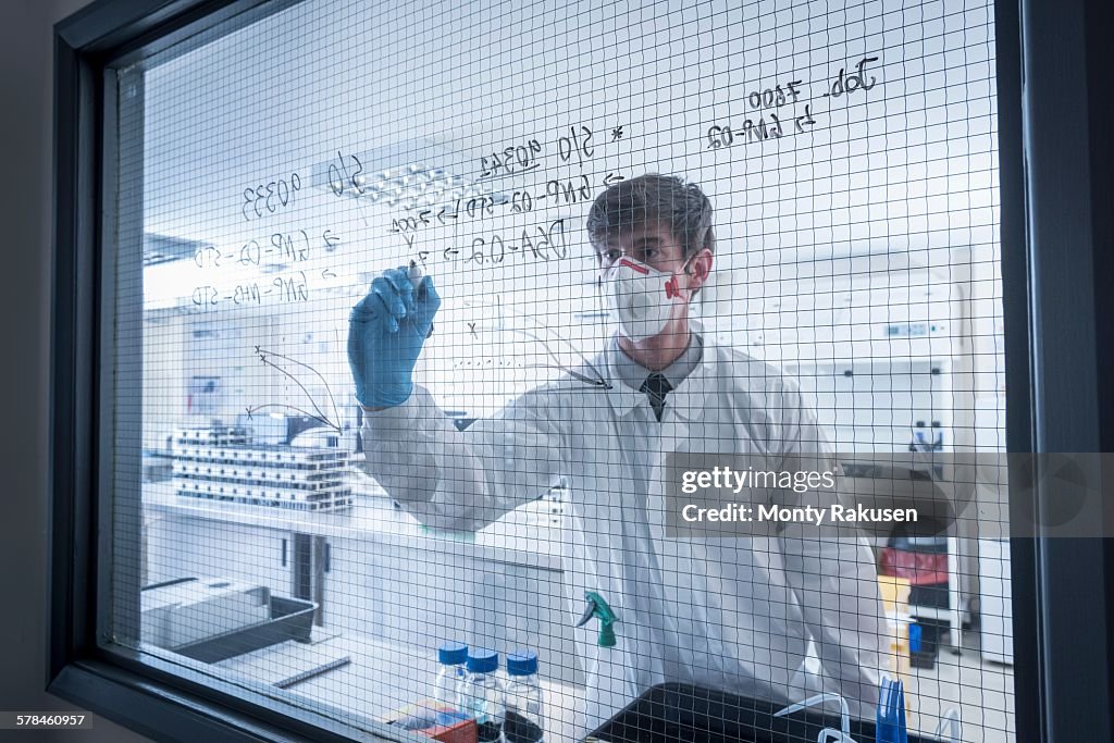 Scientist writing formulae on window of laboratory in graphene processing factory