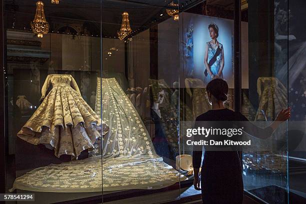 Member of Buckingham Palace staff stands next to a glass case containing Queen Elizabeth II's wedding dress during a photocall at Buckingham Palace...