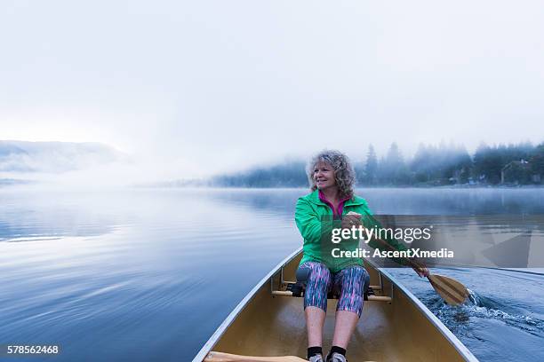 senior woman canoeing on a prisitine lake - seniors canoeing stock pictures, royalty-free photos & images