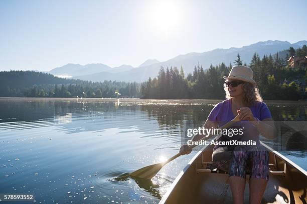 senior aged woman canoeing on a pristine lake - seniors canoeing stock pictures, royalty-free photos & images
