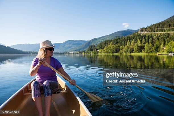 senior aged woman canoeing on a pristine lake - seniors canoeing stock pictures, royalty-free photos & images