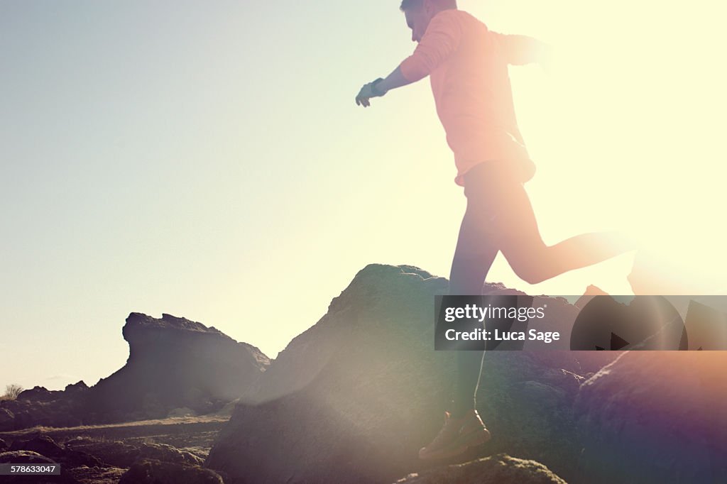 Male jumping and leaping over rocks in amazing sun