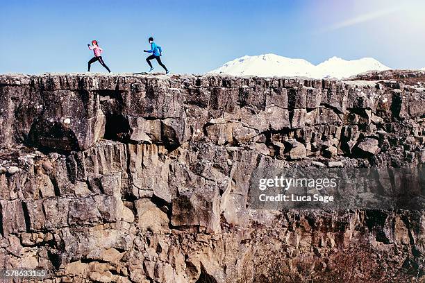 running couple run along rock edge with mountains - cliff stockfoto's en -beelden