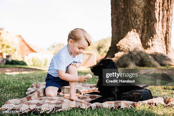 In this handout image of four released on July 22, 2016 by the Duke and Duchess of Cambridge, Prince Prince George of Cambridge feeds a cocker...