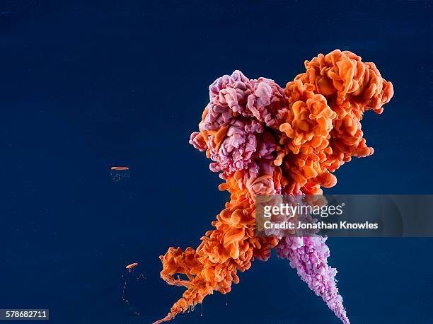 orange and purple paint in water, dark background - merger foto e immagini stock