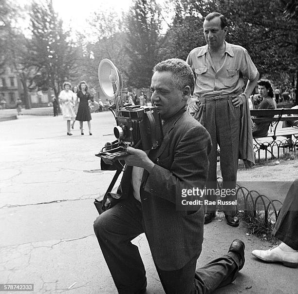 View of Austro-Hungarian born American photographer Weegee as he kneels down to line up a photograph in Washington Square Park, New York, New York,...