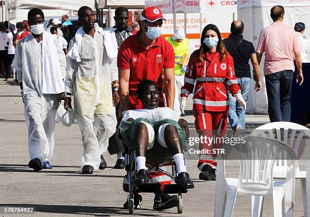 Member of the Italian Red Cross pushes a woman in a wheel chair as migrants and refugees disembark at the Trapani port on July 22, 2016 after being...