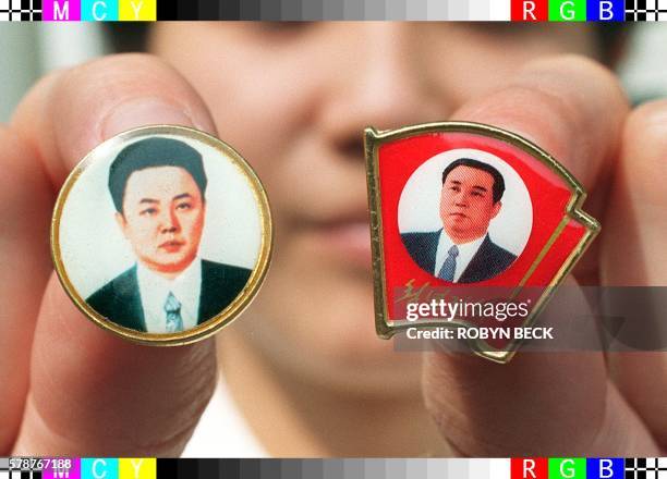 Chinese shop assistant displays badges of the late North Korean "Great Leader" Kim Il-Sung and his son and successor Kim Jong-Il which are for sale...