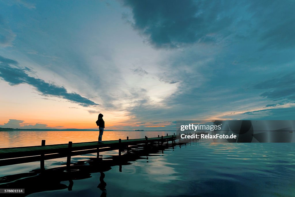 Silhouette of Woman on Lakeside Jetty with majestic Sunset Cloudscape