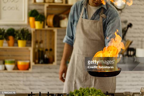 man cooking with fire in kitchen - braadpan stockfoto's en -beelden