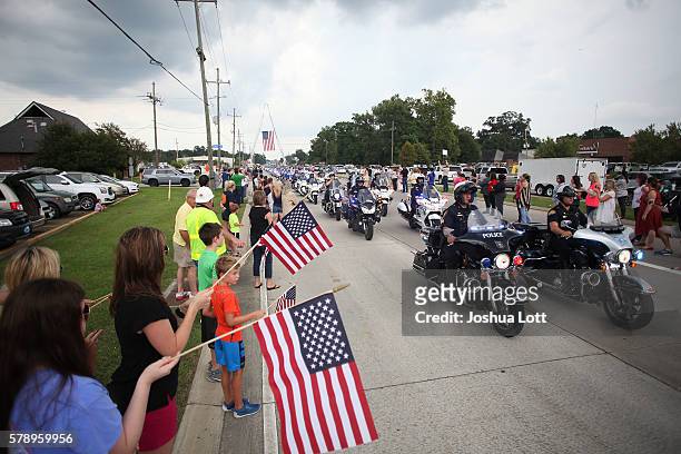 Mourners wave American flags during the funeral procession for Baton Rouge Police Officer Matthew Gerald at Healing Place Church Arena on July 22,...