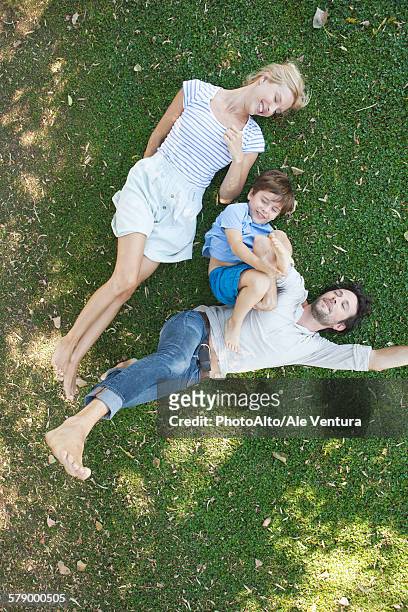 young family with boy lying together on grass - achterover leunen stockfoto's en -beelden