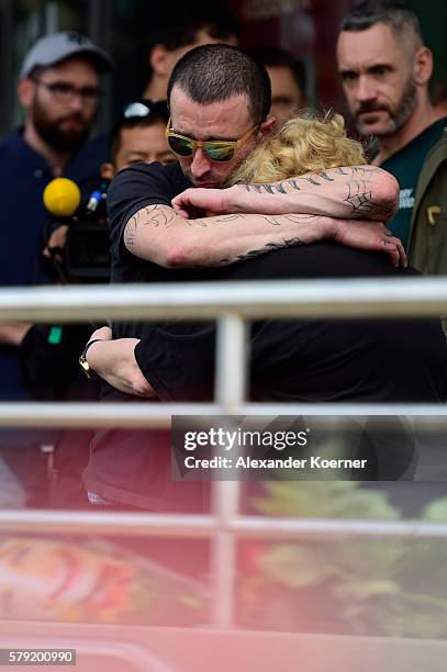 Couple takes a minute while looking at flowers and candles outside the OEZ shopping center the day after a shooting spree left nine victims dead on...