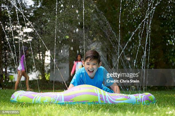 half asian boy playing on slip and slide - backyard water slide stock pictures, royalty-free photos & images