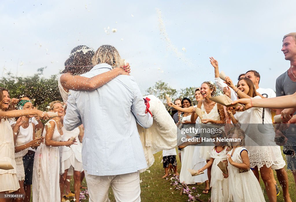 Wedding guests tossing rice at newlyweds, outdoors