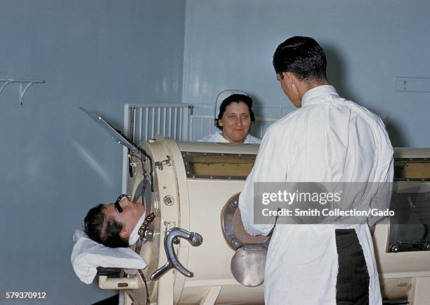 Hospital staff are examining a patient in a tank respirator, iron lung, during the Rhode Island polio epidemic, 1960. The iron lung encased the...