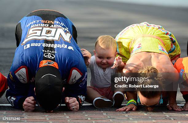 Kyle Busch, driver of the NOS Energy Drink Toyota, kisses the bricks with his wife, Samantha, and son, Brexton, after winning the NASCAR XFINITY...