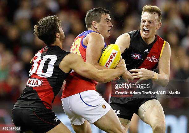 Tom Rockliff of the Lions is tackled by Kyle Langford and Brendon Goddard of the Bombers during the 2016 AFL Round 18 match between the Essendon...