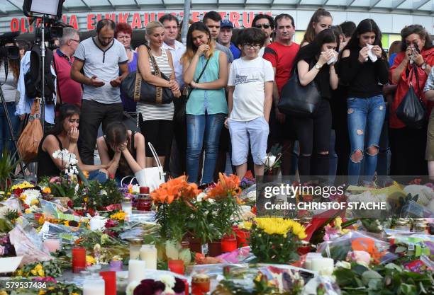 People mourn in front of candles and flowers on July 24, 2016 in front of the Olympia Einkaufszentrum shopping centre in Munich, southern Germany,...