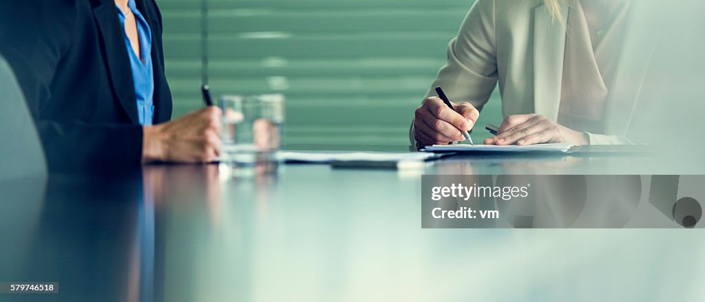 Close up of two businesswomen signing contracts at a conference