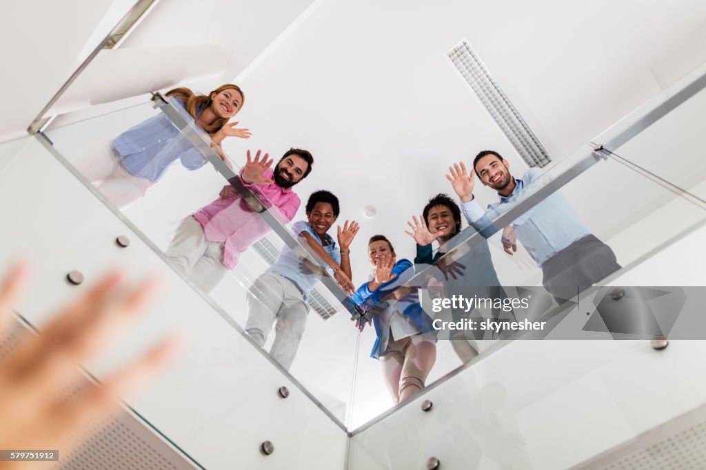 Below view of smiling business people in a hallway waving.