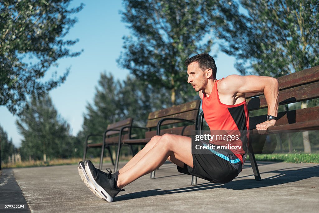 Fitness man doing bench triceps dips outdoors while working out